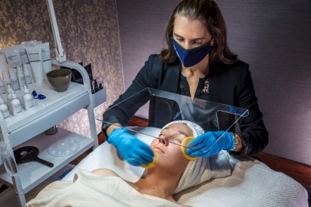 An aesthetician performs a facial on a relaxed female client.