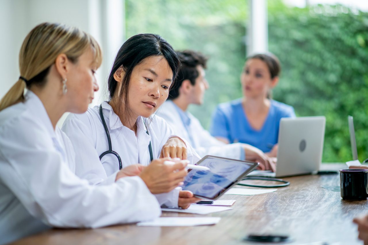 A group of medical residents prepare for ground rounds at a large conference table.