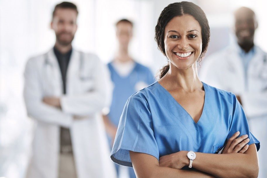 Woman in scrubs standing in front of other health care professionals.