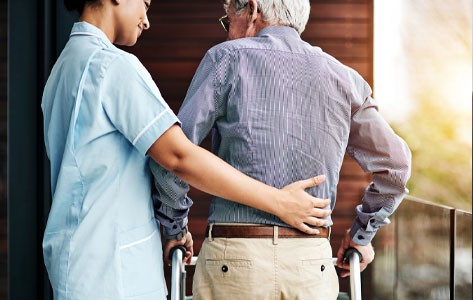 Una enfermera rodea con el brazo a un paciente mayor mientras camina con un andador.