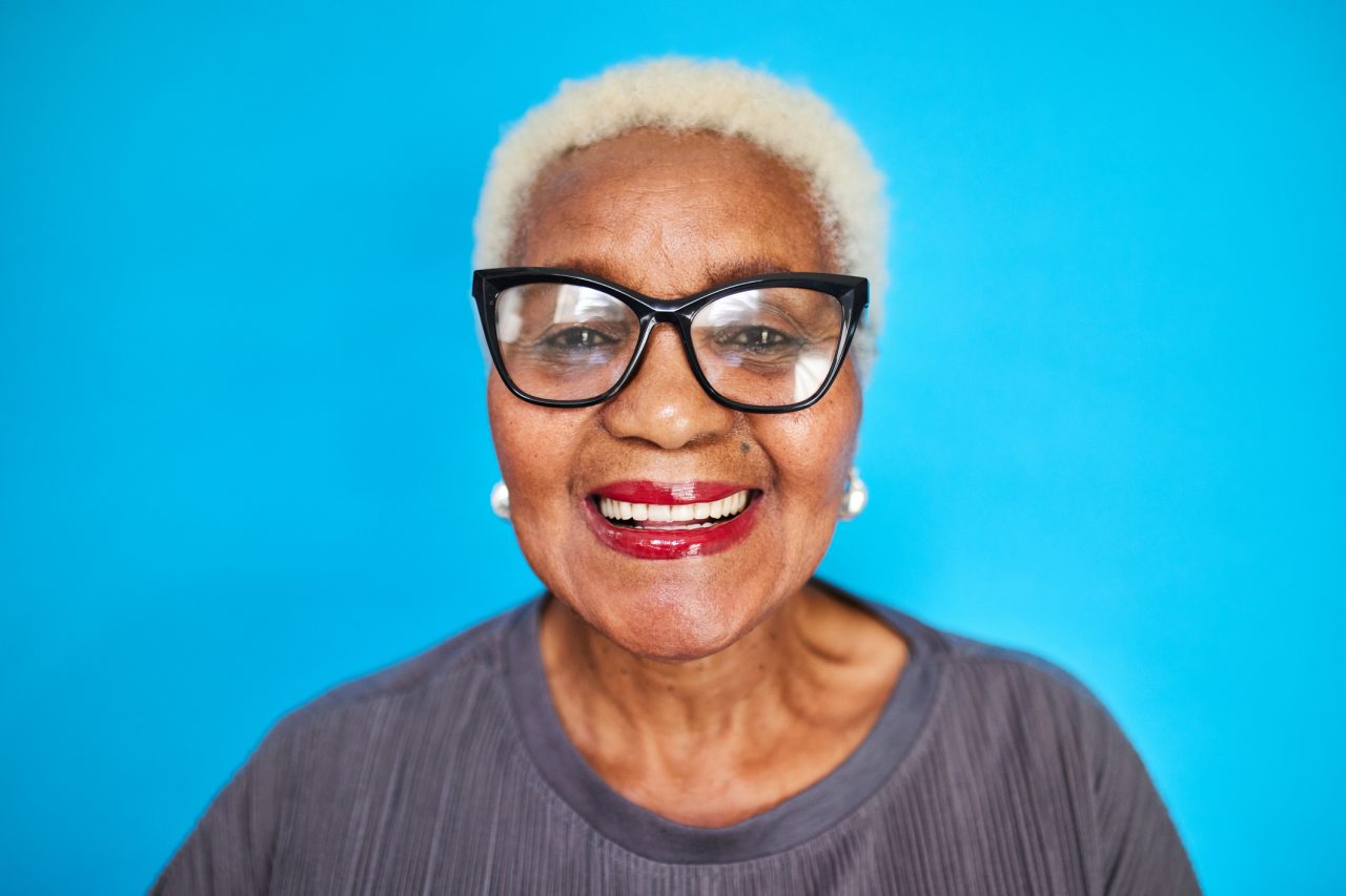 Mature black woman with bold glasses and a bright smile.
