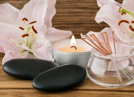 The tools of acupuncture are laid out on a table with lilies and a candle.