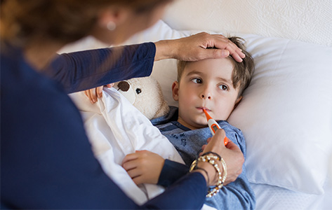 Una mamá que toma la temperatura de un niño pequeño que tiene gripe
