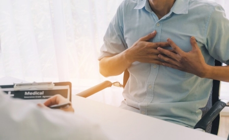 Man clutches chest at a physician's desk.