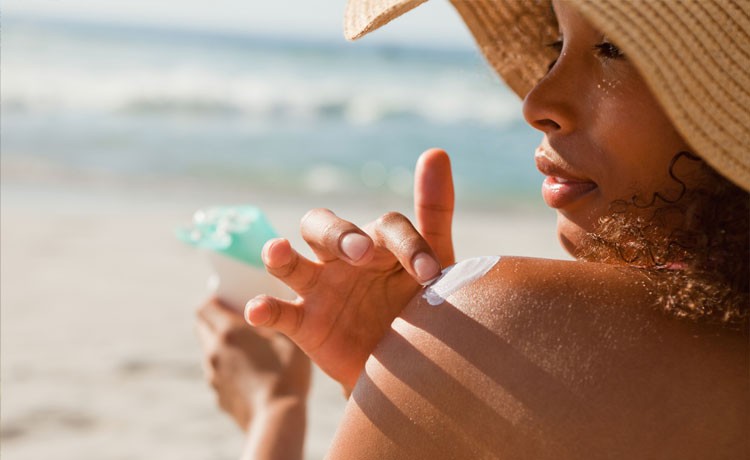A young woman at the beach applies sunscreen to keep her skin safe.
