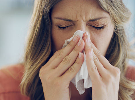 A young woman blows her nose.