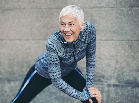 Senior woman in workout gear smiles and stretches out.