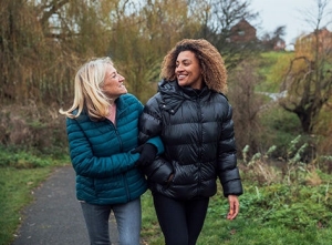 Una mujer caucásica mayor y su hija de raza mixta con ropa informal de invierno caminando por un parque local una mañana de invierno.