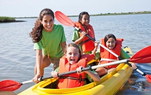 camp cousnelor and campers wearing life vests in a kayak