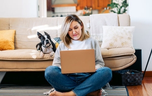 Woman using a laptop sits beside her dog