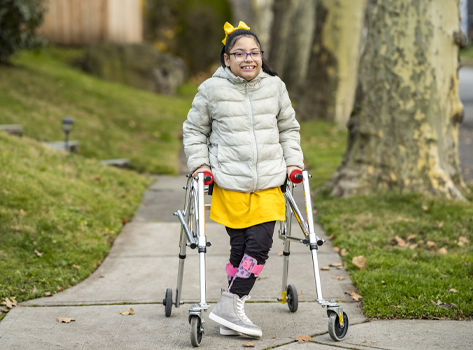 Seven-year-old Samantha E. walking down the sidewalk with help of a walker