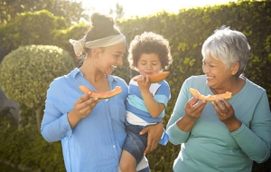 Grandmother, mother, and granchild enjoy melon on a warm summer day