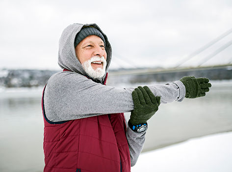 Smiling elderly man stretching outside in winter