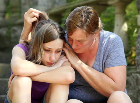 A mother comforts her distraught teenage daughter