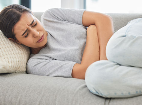 Woman laying on a couch clutching her stomach