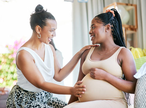 Two black women friends converse about pregnancy.