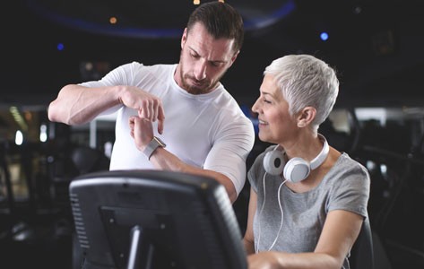 Trainer shows fitness tracker to woman on treadmill