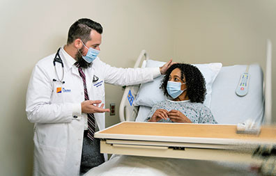 Médico hablando con paciente mientras la paciente está en la cama del hospital.