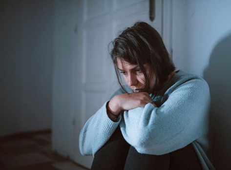 Mujer joven sentada en su habitación en la oscuridad, luchando contra la depresión.