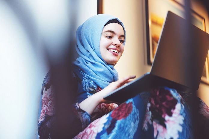 Mujer joven musulmana revisa enlaces relacionados con la salud conductual en su computadora portátil.