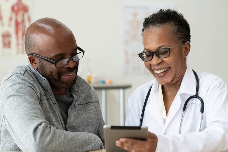 una médica le muestra los recursos sobre el cáncer a un paciente en una tableta
