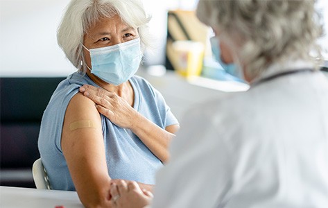 Una mujer mayor le sonríe a una enfermera después de recibir la vacuna contra la gripe.