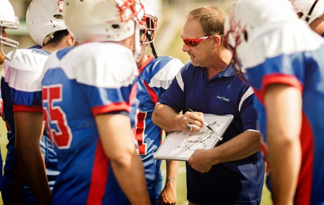 youth football coach explains the play to his players