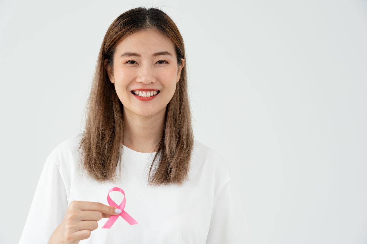 Asian woman holding a pink ribbon for breast cancer.