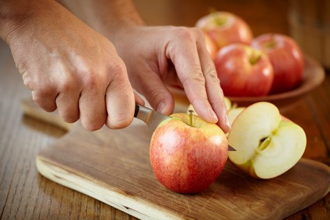 Manos cortando manzanas en una tabla de cortar