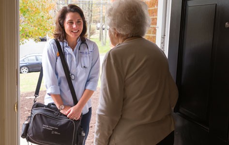 Una mujer mayor recibe en la puerta a una joven asistente de atención domiciliaria.