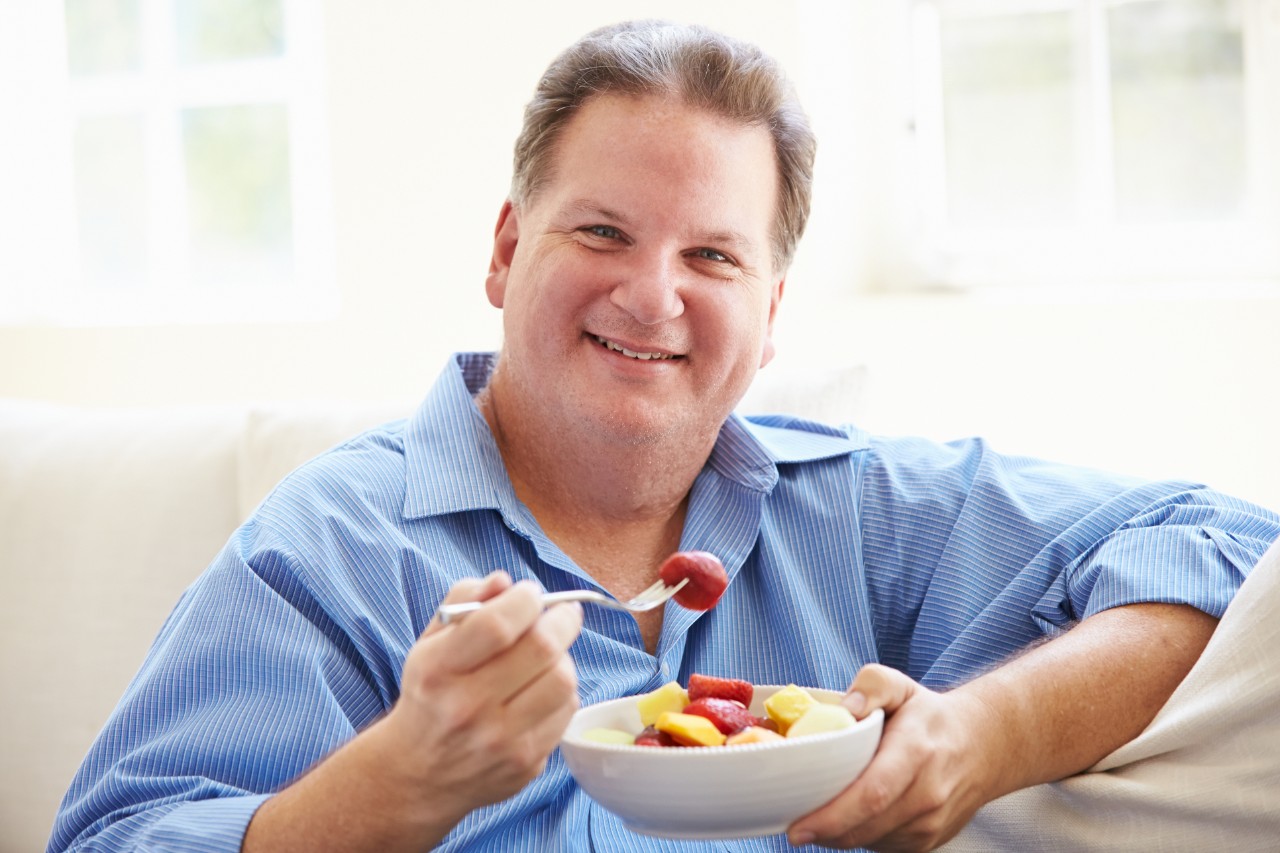 Hombre con sobrepeso comiendo fruta fresca.