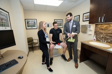 A medical consultation between male and female athletic trainers and a male athlete.
