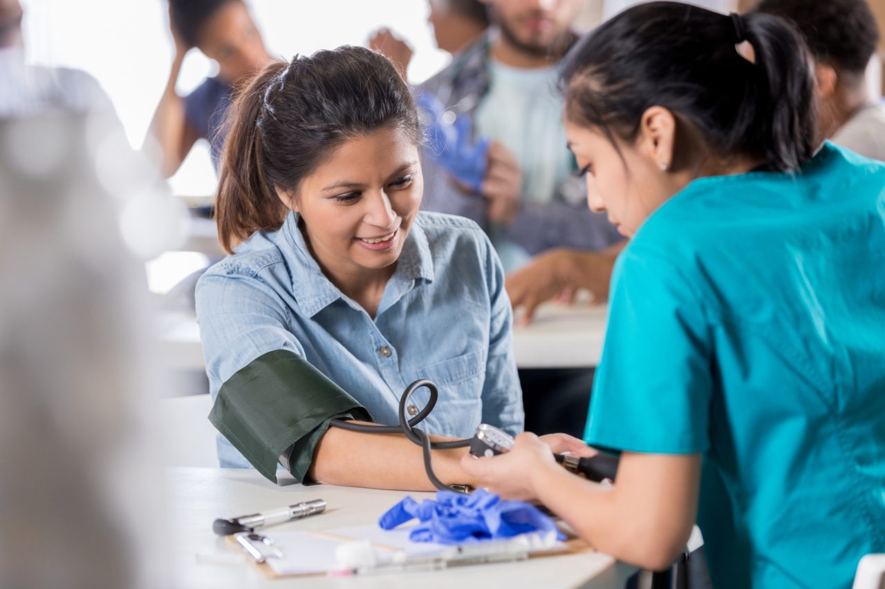 Adult woman watches as nurse takes blood pressure at a community health event.