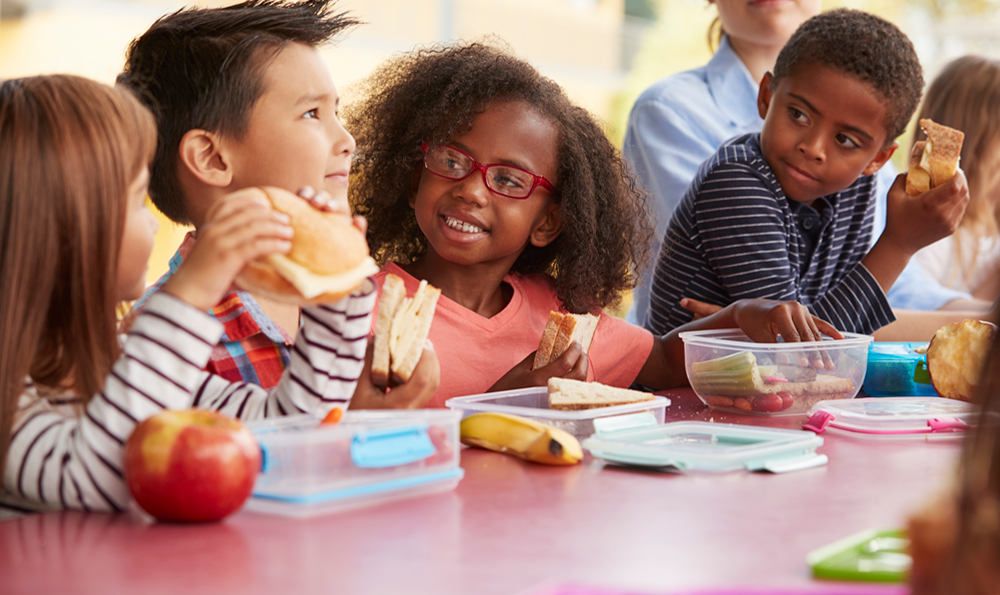 A group of elementary age children enjoy lunch in the cafeteria.
