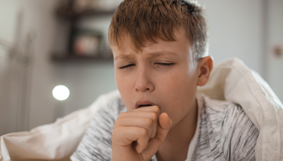 Boy with walking pneumonia coughs in bed.
