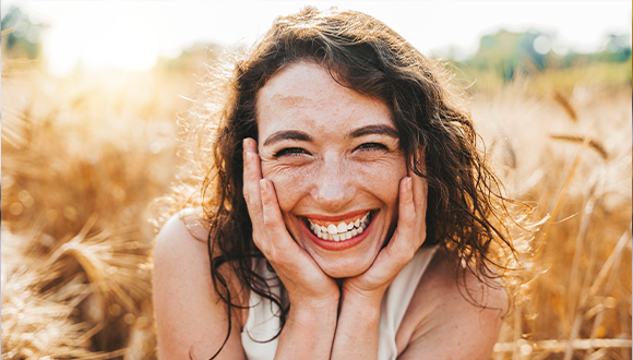 Woman in a field smiling and holding her face.
