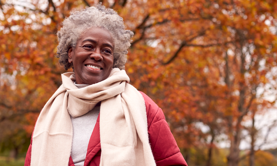 A mature African-American woman smiles while outdoors on a fall day.
