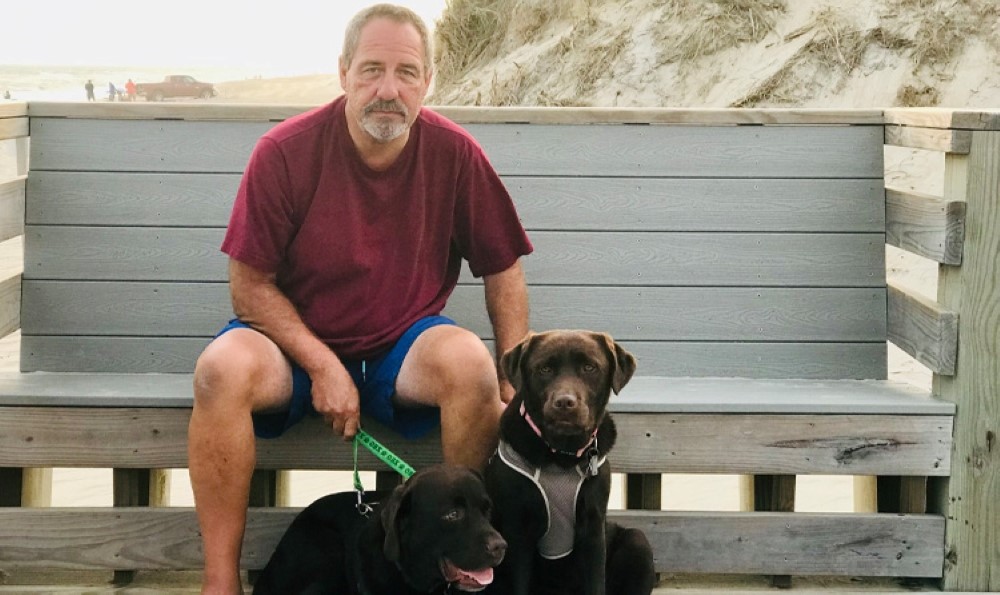 Keith sitting on a bench holding his dogs.