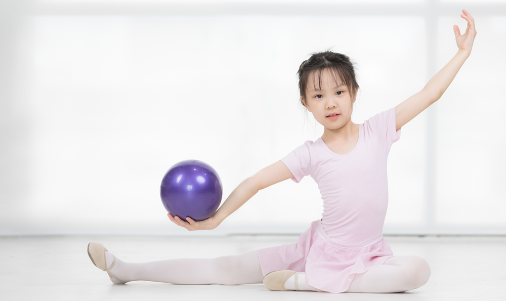 Young girl performs ballet with a purple ball.