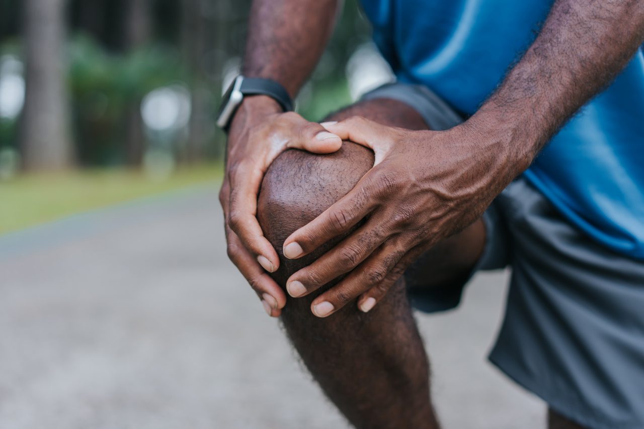 A jogging man clasps his knee in discomfort.