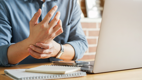 Person sitting at their work station while holding their wrist.