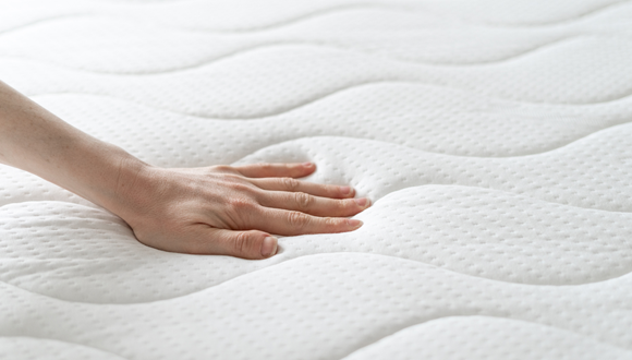 A hand is touching a mattress.