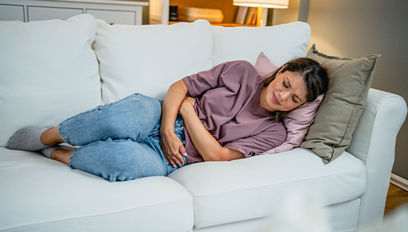 Woman laying on couch and holding her stomach.