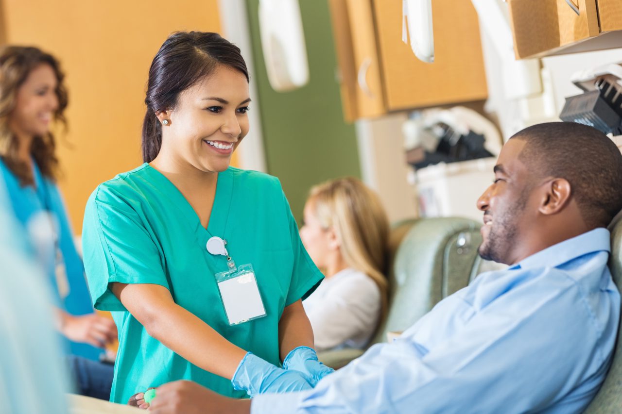 Happy nurse comforting patient while he donates blood to hospital